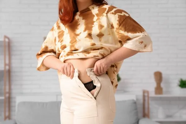 Image of woman trying to do her trousers up after pregnancy weight gain Edinburgh