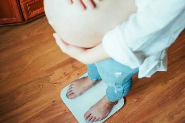 Image of woman weighing herself and experiencing weight gain through pregnancy Edinburgh